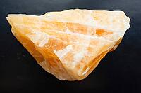 Specimen of mineral from geological collection - natural orange calcite rock close-up on black background [IBR125462113]