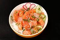 Hawaiian poke with salmon and sesame seeds, boiled rice, fresh cucumber, radish and green onions in porcelain bowl on black background. Top view. Organic seafood [IBR125462135]