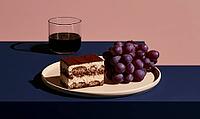 Slice of tiramisu cake beside a bunch of purple grapes. Glass of red wine sits beside plate. Plate rests on dark blue surface, AI generated [IBR125472249]