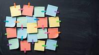 Blank colorful sticky notes with small arrow markers pointing in different directions on charcoal slate wall, indecision concept, studio shot, AI generated [IBR125472251]