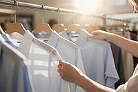 Tailored dress shirts on wooden hangers showcase modern corporate attire, curated retail fashion and white collar elegance for professional workwear, anonymous hands gently touch clean woven cotton textiles lined up on a metal clothing rack, bright mornin [IBR125472269]