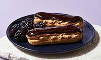 Two chocolate eclairs sit on dark plate. Blackberries beside pastries add color contrast. Plated dessert ready for serving or photography, AI generated [IBR125472290]