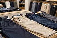 Folded trousers on a retail display table showcase menswear fashion garments and organized textile merchandising in a contemporary department store, precisely tailored cotton chinos and casual slacks arranged in alternating palettes of navy blue, warm kha [IBR125472292]