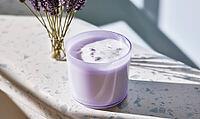 Lavender candle in glass jar on speckled surface. Bouquet of lavender flowers beside it. Natural light casts soft shadows, AI generated [IBR125472294]