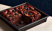 Freshly baked chocolate brownies with blackberries. Served in metal baking pan. Rich, moist texture visible. Dark background enhances warm tones, AI generated [IBR125472305]