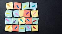 Blank colorful sticky notes with small arrow markers pointing in different directions on charcoal slate wall, indecision concept, studio shot, AI generated [IBR125472310]