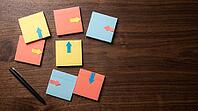 Top view of blank sticky notes with arrow markers pointing in different directions scattered on dark walnut desk beside black pen, studio shot, AI generated [IBR125472316]