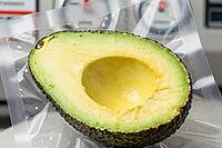 Vacuum packaging of ripe cut avocado in transparent polymer barrier film prevents enzymatic decay, controlled pressure extraction protects nutrition, textured sous vide pouch seals pitted green fruit flesh against atmospheric exposure, airtight chamber ap [IBR125472317]