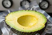 Vacuum sealed fresh avocado half in industrial plastic film showcases modified atmosphere packaging and food preservation technology, preventing enzymatic browning through oxygen elimination, stainless steel machinery featuring analog pressure gauges and  [IBR125472331]