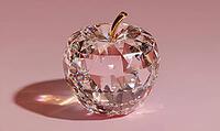 A clear apple with a gold stem sits on a pink background. The apple is made of crystal and has a shiny, reflective surface, AI generated [IBR125472336]