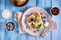 Pancakes with blueberries, sour cream and mint on a plate on the table. Homemade baking. View of mountains [IBR125492334]