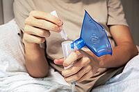 Teenage boy at home holding a nebulizer and filling it with medicine before inhalation therapy. Concept of home healthcare, respiratory disease treatment, asthma, or cold recovery. Modern medical device for breathing support [IBR125492337]