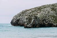 Sandy Cuevas del Mar beach with turquoise ocean water and waves breaking near large rock formations and green cliffs [IBR125492349]