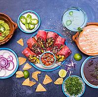 Top view of six delicious burritos, pico de gallo and traditional dishes on dark grunge surface. Tortilla chips, sliced peppers, fried beans and more on plates. Authentic Mexican cuisine [IBR125492351]