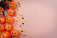 Top view of jack o lantern pumpkins, colorful candies, and toy spiders arranged on a pink background with empty space for text [IBR125492358]