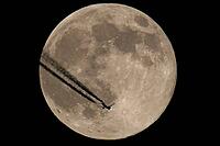 The moon and a plane in the night sky. The plane flies over the moon, against a black background [IBR125492364]