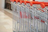 Shopping cart embedded in metal row with red handles at supermarket entrance on tile floor near checkout area displayed Organized retail access for customers [IBR125492377]