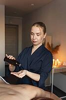 Professional masseuse pouring essential oil into hand, preparing for a calming body massage and wellness therapy session [IBR125492391]