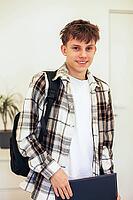 A cheerful teenager with a backpack, wearing a plaid shirt, is returning home from school. A bright and positive scene showing everyday youth life, education and extracurricular moments [IBR125492394]