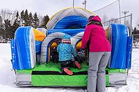 Children playing joyfully on an inflatable playground in a snowy winter park, while a parent watches nearby, enjoying the cheerful scene [IBR125492395]