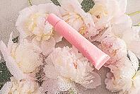 A pink plastic tube with a moisturizing balm, lip gloss, lip care mask lies on a chic background with delicate peonies and drops of water. empty package [IBR125492403]