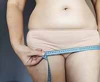 Woman measuring hips with tape measure, tracking weight loss and body transformation for health, fitness, and wellness goals [IBR125492411]