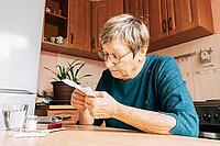 An elderly woman reads pill instructions in kitchen setting. Health maintenance, healthy aging, vitamin support, home treatment [IBR125492416]