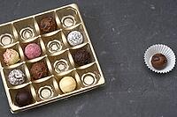 Chocolate assortment presented in square golden box on dark surface. Chocolate sweets with varied shapes and coatings, elegant pattern. premium dessert concept, holiday gift, indulgence background [IBR125492417]