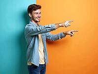 Smiling young man pointing with both index fingers to the right side of a colorful background, AI generated [IBR125502122]