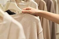 Tactile fashion retail experience with neutral beige knitwear on hangers, a customer hand touches soft wool textiles in a quiet luxury boutique, delicate fingers gently examining the knit structure of an understated beige sweater on a minimalist hanger co [IBR125502124]