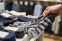 Tactile evaluation of knitted hosiery on a retail display table highlights sensory consumerism and material quality inspection, a human hand carefully grasps a patterned wool blend sock while assessing fabric texture and woven elasticity, neatly stacked g [IBR125502129]