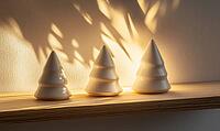 Three small white ceramic Christmas trees on a light wooden shelf, illuminated by soft natural light, casting gentle shadows, AI generated [IBR125502138]