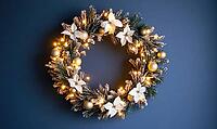 Elegant round holiday wreath with white and gold decorations against a matte dark blue wall, tiny warm lights on the wreath adding a cozy glow, AI generated [IBR125502149]