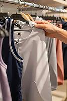Athletic garment selection in modern retail fashion boutique, tactile consumer decision browsing sportswear textile materials on hanger racks, human hand reaching out to inspect smooth synthetic microfiber fabric of a zip jacket, functional sportswear gar [IBR125502156]