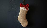 Simple beige stocking with a single red bow and white trim, hanging against a dark gray wall, AI generated [IBR125502185]