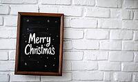 A plain black chalkboard with Merry Christmas written in white chalk, leaning against a white brick wall with, AI generated [IBR125502209]