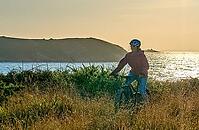 Active senior woman cycling with her electric mountain bike along the wild atlantic coast of Finisterre at Cape Frehel, Brittany, France [IBR125521080]