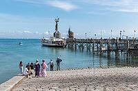 Visitors stand on the stone promenade and watch the ship at the sunny pier, harbor with the Imperia statue, Constance on Lake Constance, Baden-Württemberg, Germany [IBR125521084]