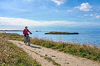 Active senior woman cycling with electric mountain bike along the wild atlantic coast of Quiberon Peninsula, Brittany, France [IBR125521103]