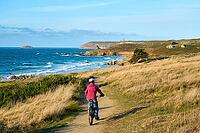 Active senior woman cycling with her electric mountain bike along the wild atlantic coast of Finisterre at Cape Frehel, Brittany, France [IBR125521119]
