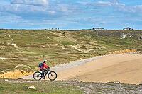 Active senior woman cycling with her electric mountain bike along the wild coast of Finisterre in southern Brittany next to Camaret-sur-Mer, France [IBR125521121]