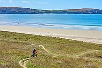 Active senior woman cycling with her electric mountain bike along the wild coast of Finisterre in southern Brittany next to Camaret-sur-Mer, France [IBR125521123]