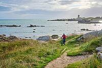 Nice senior woman cycling with her electric mountain bike at the rocky rose granite coast at Meneham site in Kerouarn, Brittany, FranceKerouarn [IBR125521136]