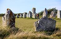 Woman cycling between the neolithic menhirs of Camaret sur mer in Brittany, France [IBR125521141]