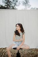 Brown-haired girl, 11, sitting on a stool in a cornfield against a beige background [IBR125521146]
