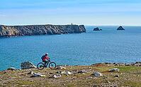 Active senior woman cycling with her electric mountain bike along the wild coast of Finisterre in southern Brittany next to Camaret-sur-Mer, France [IBR125521148]