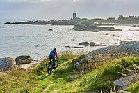 Nice senior woman cycling with her electric mountain bike at the rocky rose granite coast at Meneham site in Kerouarn, Brittany, FranceKerouarn [IBR125521153]