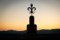 A Fleur-de-lis symbol, stylized lily, stands out as a dark silhouette against the orange sunset and a mountain range, Gubbio, Umbria, Italy [IBR125521160]