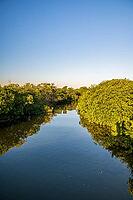 Vertical landscape photo of a tranquil water channel surrounded by dense green mangroves in Sian Ka'an Biosphere Reserve, Quintana Roo, Mexico. The calm water reflects the vegetation and the clear blue sky above, creating a peaceful tropical wetland scene [IBR125527049]
