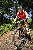 Mountain biker riding a root trail in the forest. Frontal view. Zurich Oberland, Switzerland [IBR125527061]